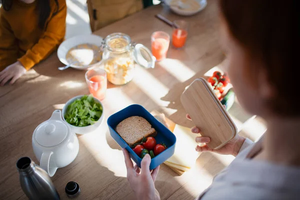 Close-up of mother preparing snack to lunch box in kitchen at home. — Stock Photo, Image