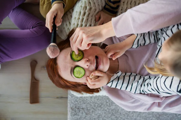 Pouco chidlren colocando pepino no rosto de suas mães e aplicando maquiagem para ela em casa. — Fotografia de Stock