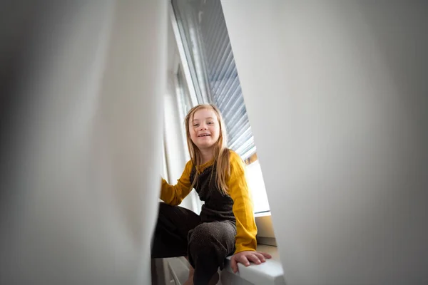 Glückliches kleines Mädchen mit Down-Syndrom sitzt zu Hause am Fenster. — Stockfoto