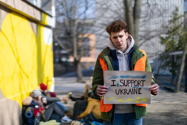 Tiltakozom Ukrajna orosz megszállása ellen. Férfi önkéntes, aki háborús zászlót tart a menekülttábor közelében.. — Stock Fotó