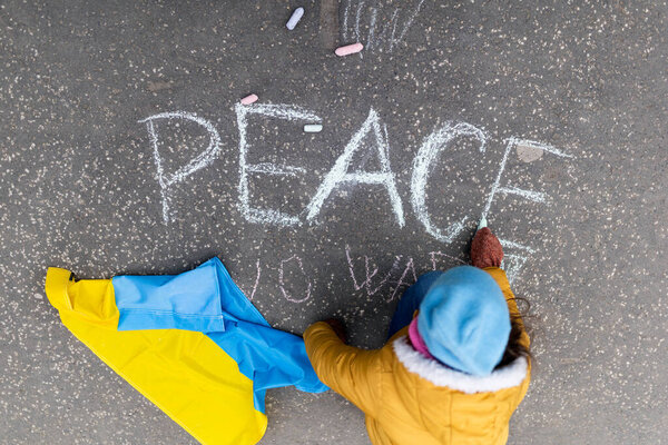 Top view of little girl writing peace with chalk. Protest against Russian invasion of Ukraine.