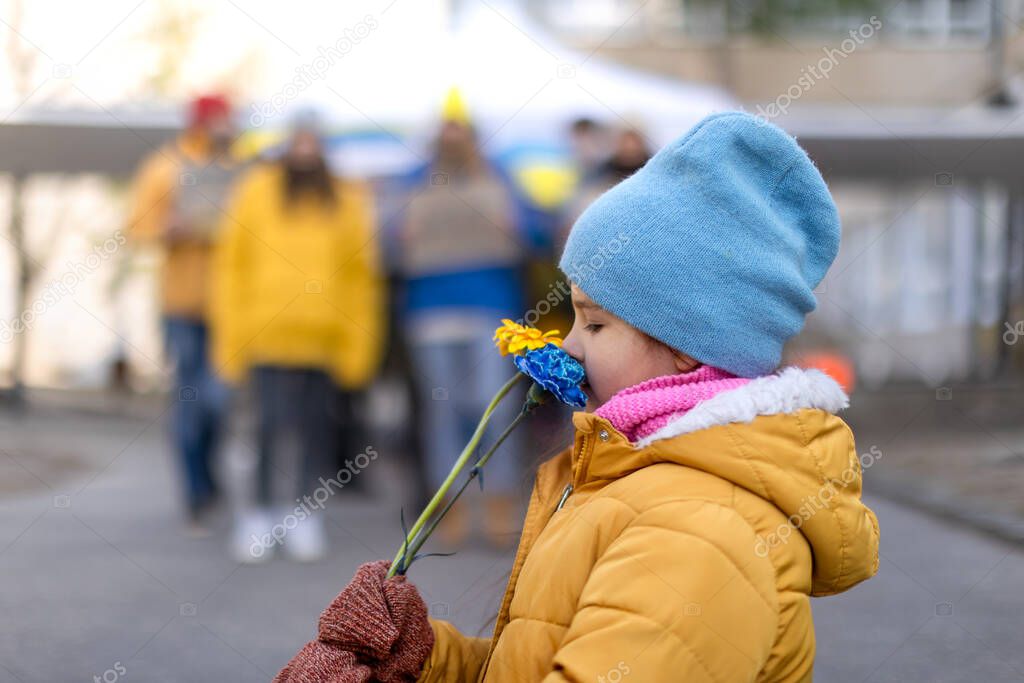 LIttle girl holding yellow and blue flowers. Protest against Russian invasion of Ukraine.