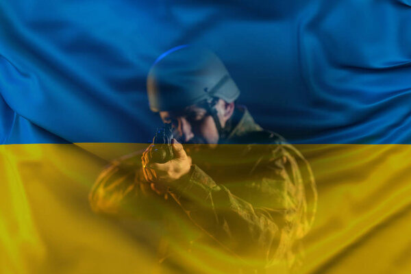 Double exposure of doldier in military uniform and helmet aiming with weapon to camera and Ukrainian flag.