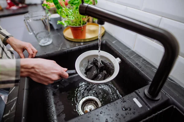 Frau reinigt Schungit-Steine in Sieb mit Gießwasser in Spüle. — Stockfoto