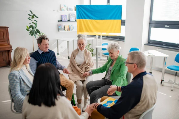 Idősek csoportja fogja egymás kezét és imádkozik Ukrajnáért a templomi művelődési házban.. — Stock Fotó