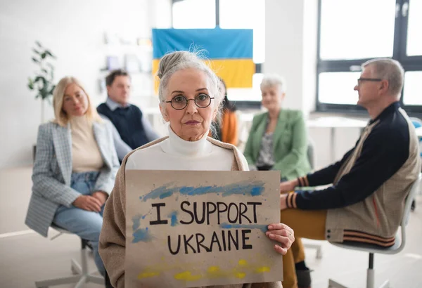 Group of seniors showing support when praying for Ukraine together in church community center.