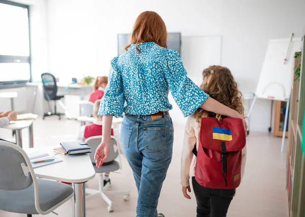 Vista posteriore di insegnante con studentessa ucraina in classe, concetto di iscrizione bambini ucraini a scuole. — Foto Stock