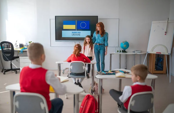 Profesor dando la bienvenida a la colegiala ucraniana en el aula, concepto de inscribir a niños ucranianos en escuelas. — Foto de Stock
