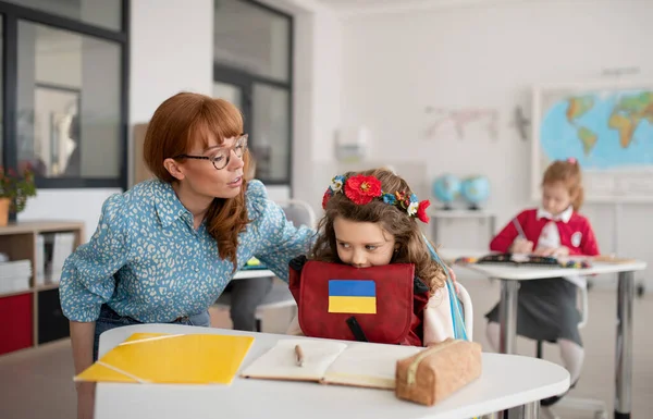 Leraar met Oekraïense schoolmeisje in de klas, concept van het inschrijven van Oekraïense kinderen naar scholen. — Stockfoto