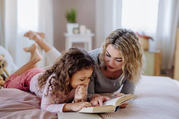 Щаслива мати зі своєю маленькою донькою лежить на ліжку і читає книгу вдома . — стокове фото