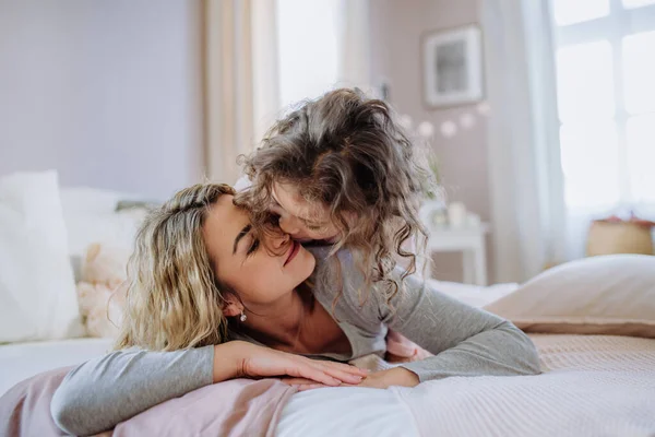 Счастливая мать со своей маленькой дочерью обнимается и веселится вместе в постели дома. — стоковое фото