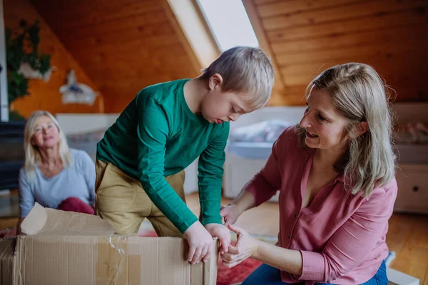 Niño con síndrome de Down con su madre y su abuela jugando con la caja juntos en casa. — Foto de Stock