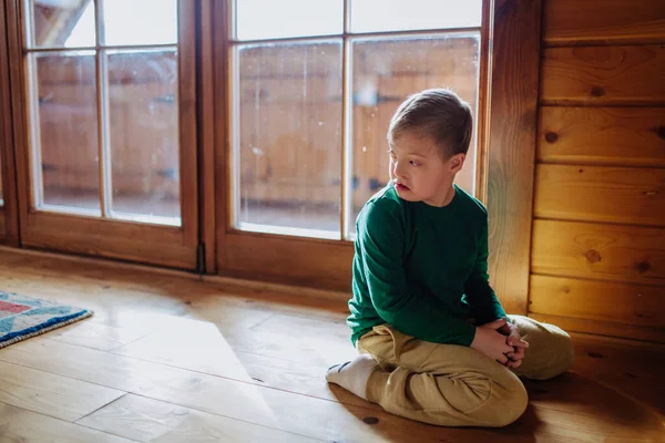 다운 증후군 이 있는 슬픈 소년 이 집 바닥에 앉아 있는 모습. — 스톡 사진