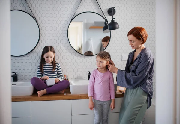 Mutter bürstet ihren kleinen Töchtern Haare im Badezimmer, Morgenroutine-Konzept. — Stockfoto