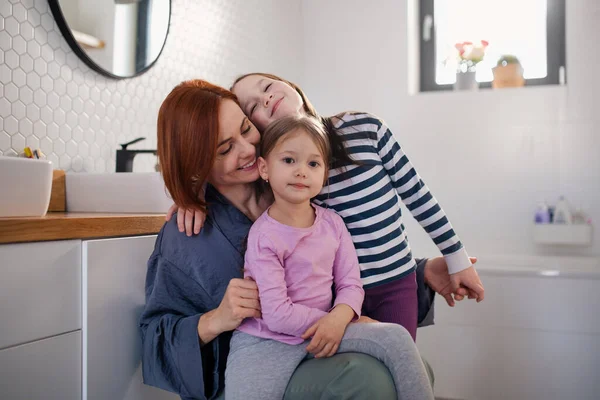 Мати двох маленьких дівчат обіймає їх у ванній вдома . — стокове фото