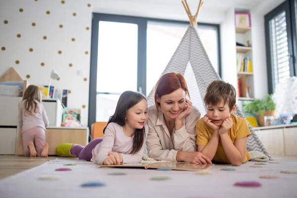 Cheerful mother of three little children reading them book at home. — Stock Photo, Image