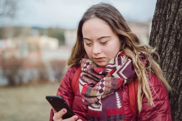 Jonge vrouw met Down syndroom lopen in de straat in de winter en met behulp van smartphone — Stockfoto