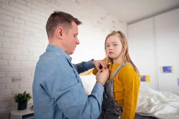 Far hjälper sin lilla dotter med Downs syndrom att bära byxor hemma. — Stockfoto