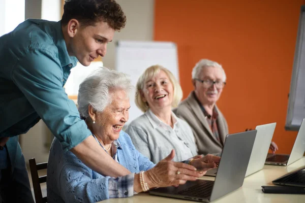 Groupe de personnes âgées dans une maison de retraite avec un jeune instructeur apprenant ensemble en classe d'informatique — Photo