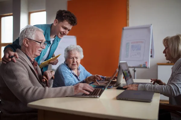 Seniorengruppe im Altenheim mit jungem Lehrer lernt gemeinsam im Computerkurs — Stockfoto