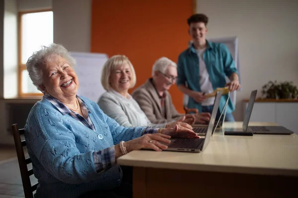 Seniorengruppe im Altenheim mit jungem Lehrer lernt gemeinsam im Computerkurs — Stockfoto