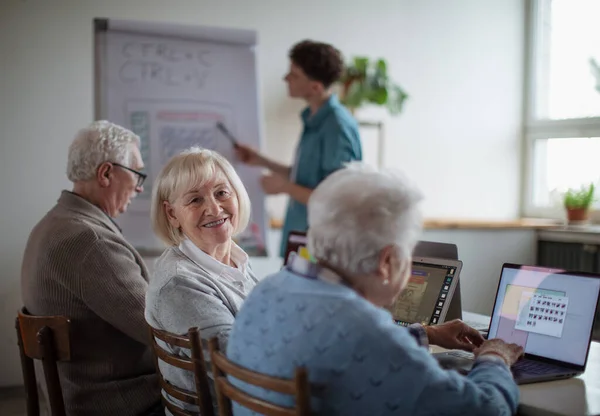 Старшая группа в доме престарелых вместе с молодым инструктором, обучающимся в компьютерном классе — стоковое фото