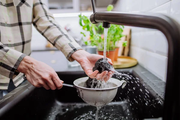 Frau reinigt Schungit-Steine in Sieb mit Gießwasser in Spüle. — Stockfoto