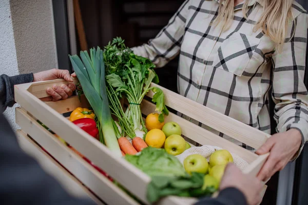 Mann hält Kiste mit Gemüse und Obst und übergibt sie der Frau, die vor der Tür steht. — Stockfoto