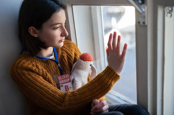 Trauriges ukrainisches Flüchtlingsschulmädchen, das zu Hause fehlt und aus dem Fenster schaut. Ukrainisches Kriegskonzept. — Stockfoto