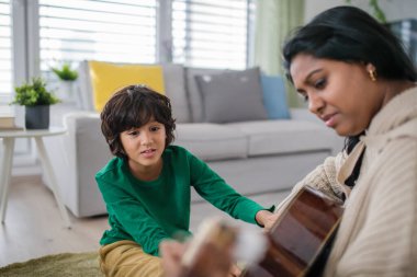 Küçük çok kültürlü çocuk evde annesiyle gitar çalmayı öğreniyor..