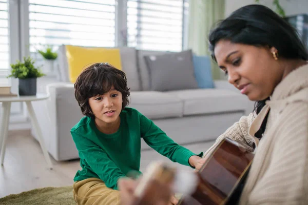 Piccolo ragazzo multirazziale che impara a suonare la chitarra con sua madre a casa. — Foto Stock