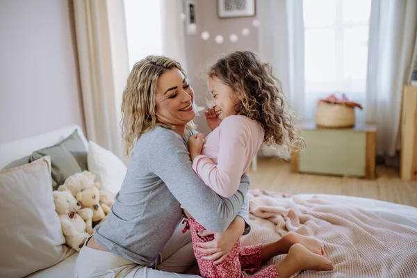 Щаслива мати зі своєю маленькою дочкою обіймається і розважається разом у ліжку вдома . — стокове фото