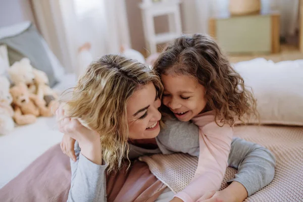 Щаслива мати зі своєю маленькою дочкою обіймається і розважається разом у ліжку вдома . — стокове фото