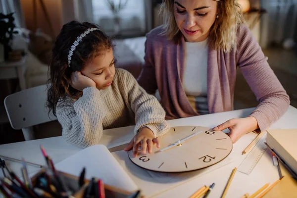 Счастливая маленькая девочка учится с деревянными часами вместе с мамой вечером дома. — стоковое фото