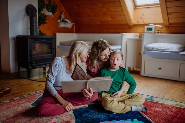 Annesi ve büyükannesiyle Down sendromlu bir çocuk evde aile fotoğrafı albümüne bakıyor.. — Stok fotoğraf