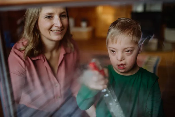 Jongen met Down syndroom met zijn moeder schoonmaken venster thuis. — Stockfoto