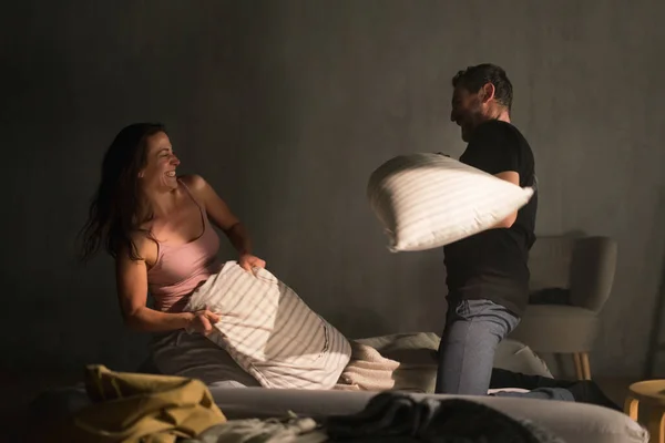 Casal feliz batendo com travesseiros na cama em um quarto em casa. — Fotografia de Stock