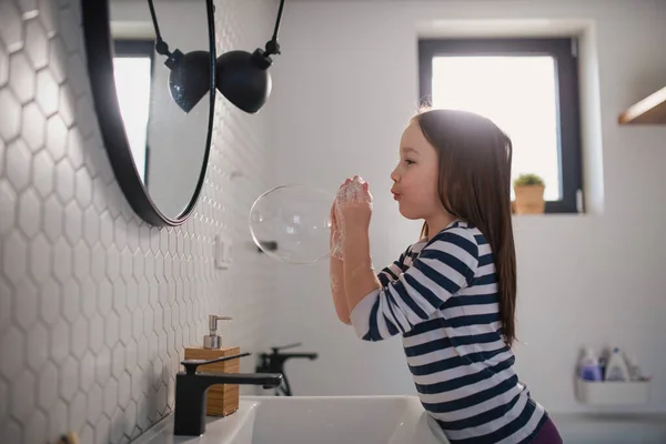 Niña en el baño, lavándose las manos y haciendo burbujas de jabón. — Foto de Stock