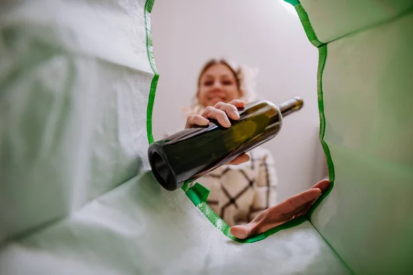 Image from inside green recycling bag of woman throwing a glass bottle to recycle. — Stock Photo, Image
