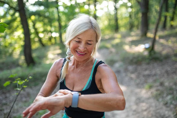 Porträt einer aktiven Seniorin, die draußen im Wald steht und eine Smartwatch aufsetzt. — Stockfoto