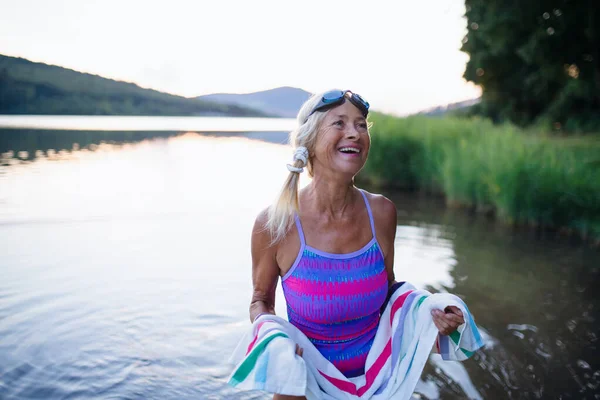 Porträt einer aktiven Seniorenschwimmerin, die sich im Freien am See mit Handtuch trocknet. — Stockfoto