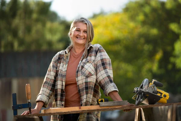 Feliz carpintero femenino práctico que trabaja en taller de carpintería al aire libre con sierra circular — Foto de Stock