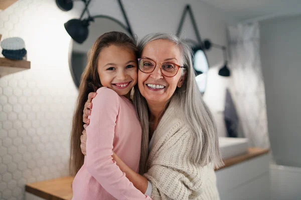 シニア祖母と孫娘がバスルームに室内に立って、抱き合ってカメラを見て. — ストック写真