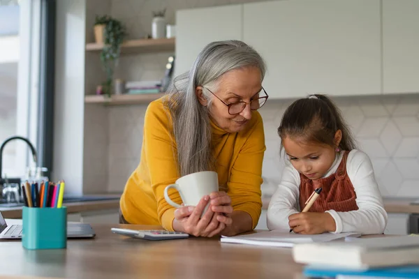 Klein meisje met senior oma doet huiswerk thuis. — Stockfoto