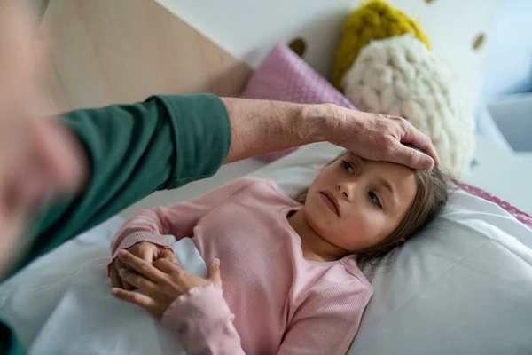 Grootvader zorgt voor zijn zieke kleindochter in bed. — Stockfoto