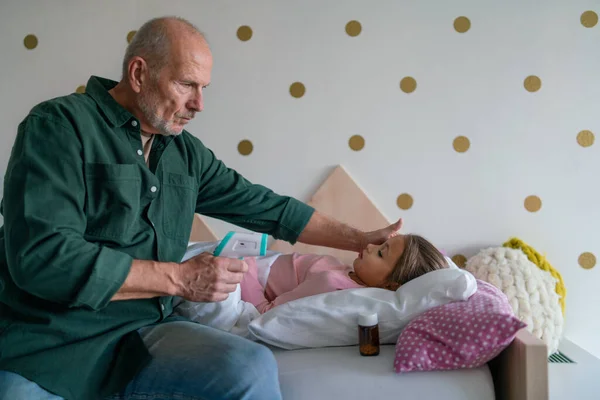 Grand-père prenant soin de sa petite-fille malade couchée au lit. — Photo