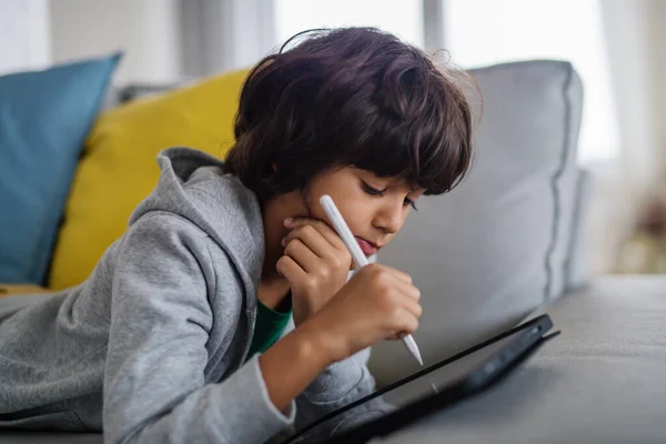 Pequeño chico multirracial con la tableta acostado en el sofá en casa. — Foto de Stock