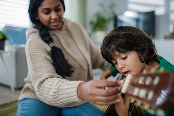 Pequeño chico multirracial aprendiendo a tocar la guitarra con su madre en casa. — Foto de Stock