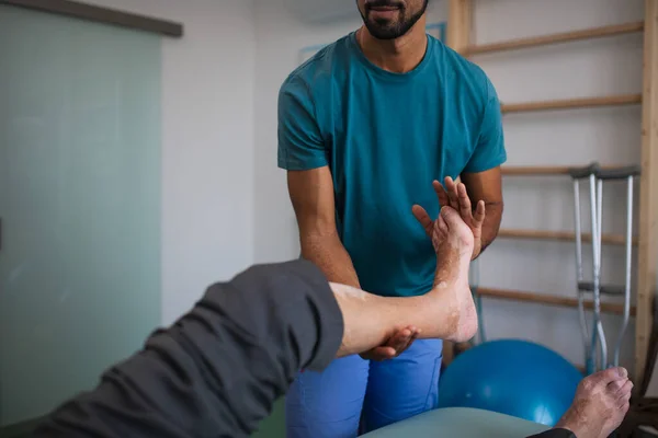 Primo piano del fisioterapista che esercita con i pazienti anziani gamba in una stanza fisica. — Foto Stock