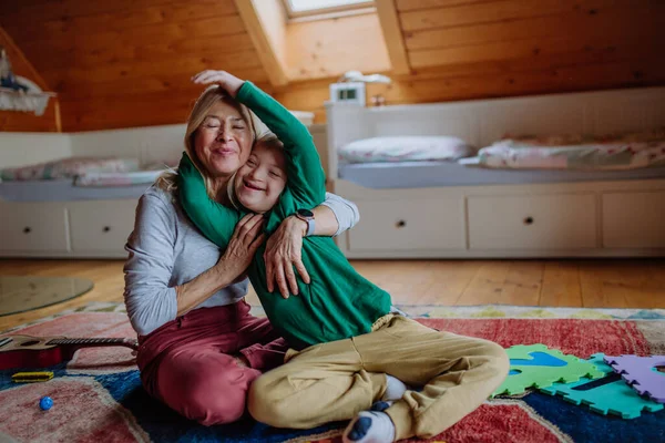 다운 증후군 이 있는 행복 한 소년 이 바닥에 앉아 집에서 할머니와 포옹하는 모습. — 스톡 사진